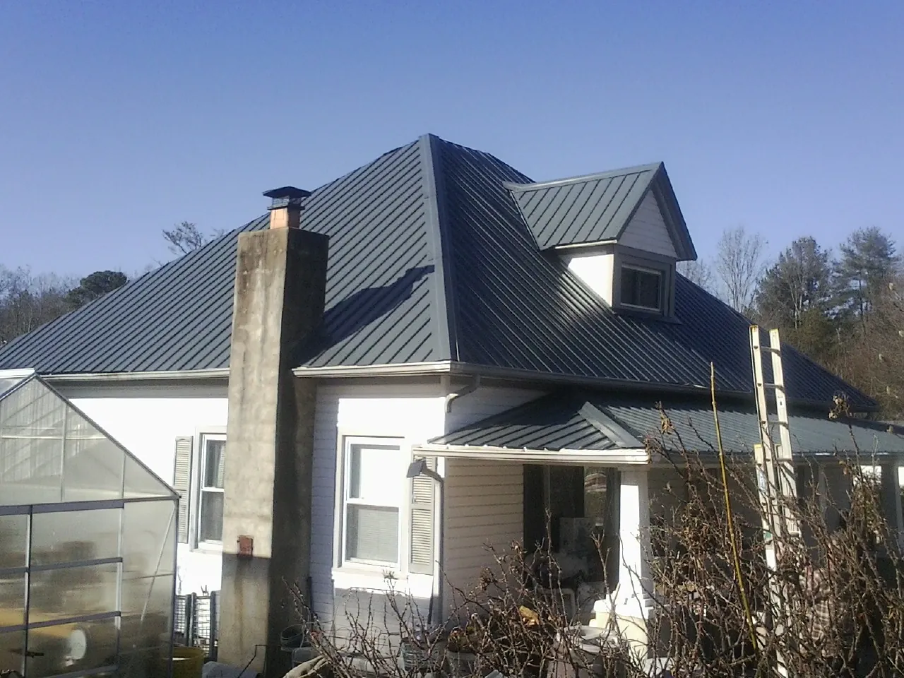Dark blue standing seam metal roof on a white farmhouse with dormer — Slate & Tile Roof Repair by Roofing Brothers in Minturn