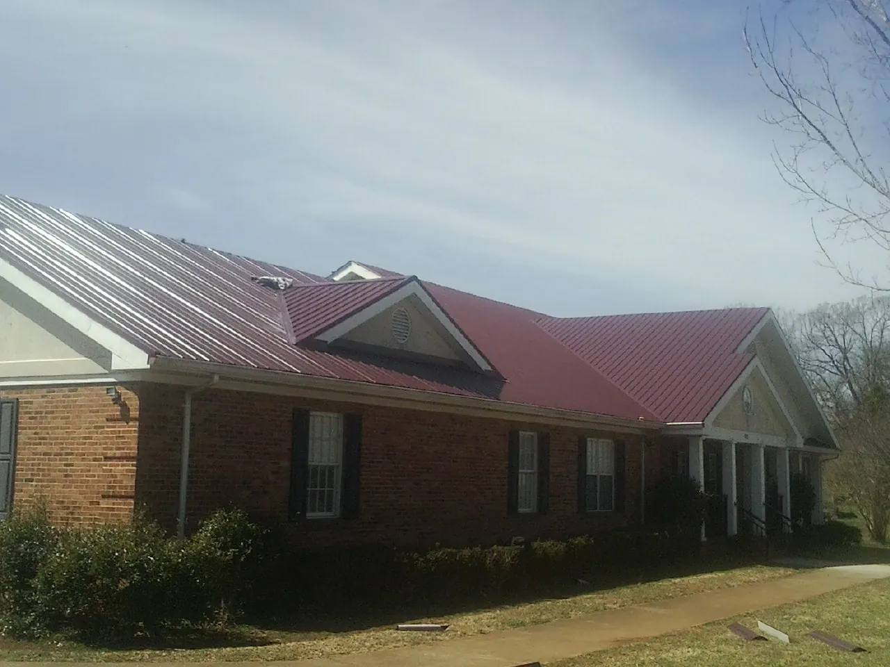 Red metal roof with gabled entries on a long brick building, from a Hail Damage Roof Repair job in Minturn