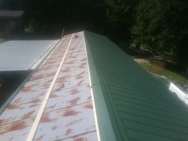 Old rusted panels beside newly installed green metal roofing — Wind Damage Roof Repair by Roofing Brothers in Minturn