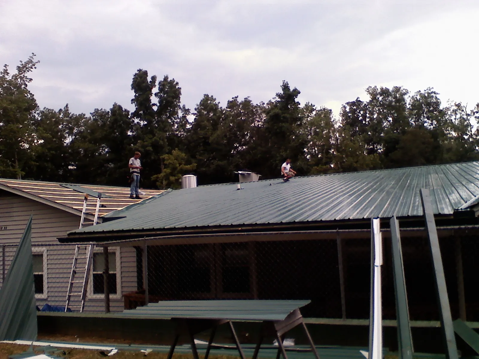 Two roofers installing green metal panels above a covered porch in Minturn