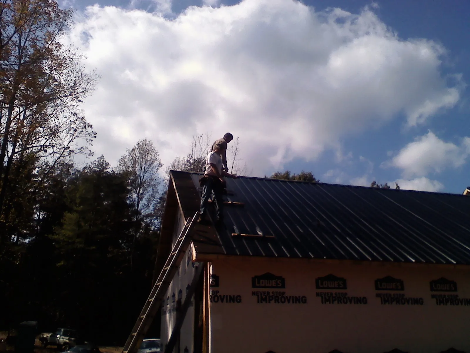 Roofer fastening dark metal panels high against a cloudy sky, from a Roof Inspection job in Minturn